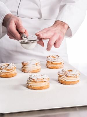 Chef ajoute du sucre sur des Paris-Brest